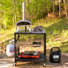 an outdoor stove and grill on the ground in front of some trees, with a bag next to it