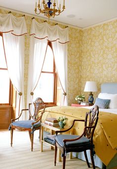 a bed room with a neatly made bed next to two chairs and a chandelier