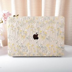 an apple computer case sitting on top of a white table next to a pink flower