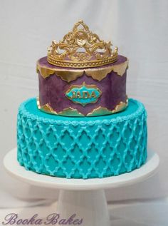 a three tiered cake decorated with blue and purple icing, topped with a gold crown