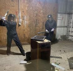 two men in black suits and helmets are holding baseball bats while standing next to a trash can