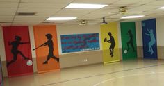 an indoor basketball court with colorful banners on the wall and painted silhouettes of players