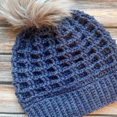 a knitted hat with a pom - pom on the top, sitting on a wooden surface