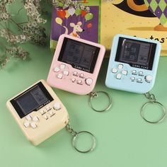 three gameboy keychains sitting next to each other on a green surface with flowers in the background