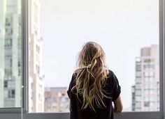 a woman standing in front of a window looking out at the cityscape and skyscrapers