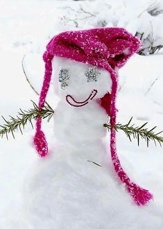 a snowman wearing a pink hat and scarf in the snow with pine needles sticking out of it