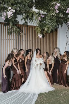 a group of women standing next to each other in front of a wooden fence with flowers on it