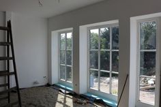 an empty room with three windows and a ladder on the floor in front of them