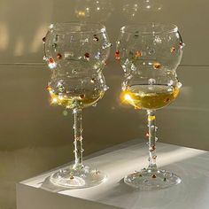 two wine glasses sitting next to each other on a white counter top with lights in them