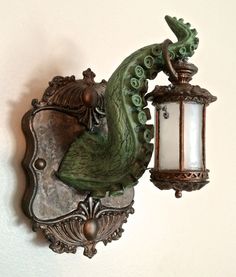 a wall mounted light with a green dragon on it's back and an old fashioned lamp hanging from the side