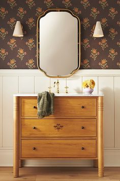 a wooden dresser with a mirror above it and two lamps on the wall behind it