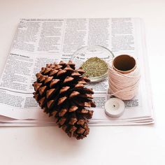 a pine cone sitting on top of a newspaper next to a spool of thread