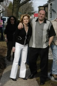 a man and woman standing next to each other on a sidewalk with people in the background