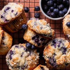 blueberry muffins on a cooling rack next to a bowl of blueberries