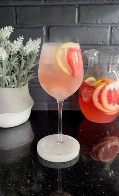 two wine glasses filled with pink lemonade and grapefruit on a black counter