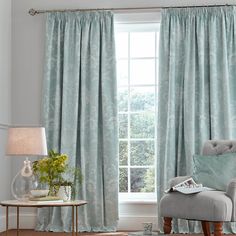 a living room filled with furniture and a window covered in blue drapes, sitting next to a chair