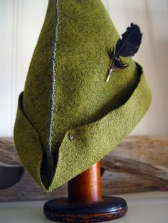 a green hat with a feather resting on it's brimmed cap, sitting on top of a wooden stand