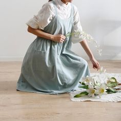 a woman kneeling on the floor with flowers in her hand and wearing a blue dress