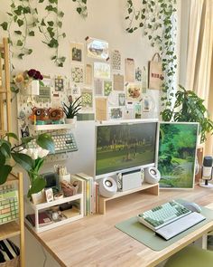 there is a computer on the desk in front of some plants and pictures hanging on the wall