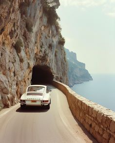 a white car driving down a road next to a cliff