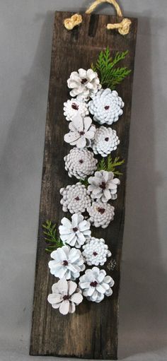 a wooden sign with pine cones and white flowers on the front, hanging from a rope