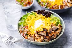 two bowls filled with chicken, black beans and cheese next to a glass of water