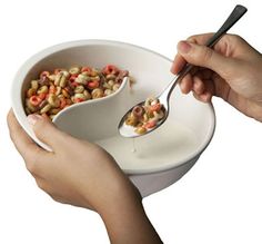 two hands holding spoons over a bowl filled with cereal