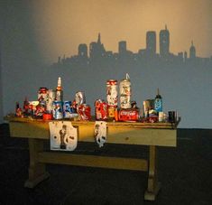 a wooden table topped with lots of different types of soda bottles and cans in front of a city skyline