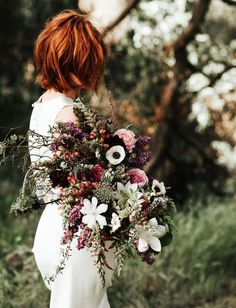 a woman with red hair holding a bouquet of flowers and greenery in her hands