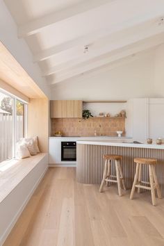 an open kitchen with wooden floors and white counter tops, along with two stools