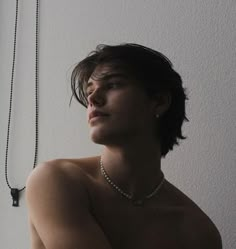 a shirtless man wearing a pearl necklace and pearls around his neck, standing in front of a white wall