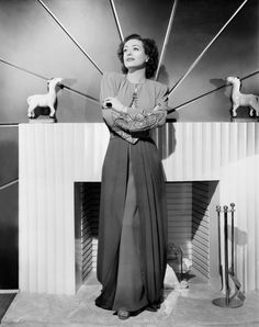 an old photo of a woman standing in front of a fireplace with sheep on the mantle