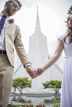 a man and woman holding hands in front of a building with a spire on it