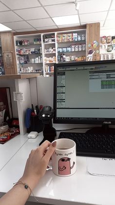 a person is holding a coffee mug in front of a laptop computer on a desk