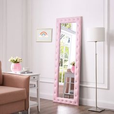 a pink mirror sitting on top of a wooden floor next to a chair and table