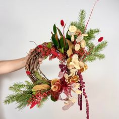 a person holding a wreath with flowers and greenery on it in front of a white background