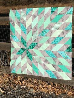 a green and white quilt sitting on top of a wooden fence