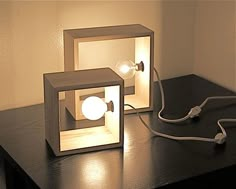 two cube shaped lamps sitting on top of a wooden table next to a lamp plugged in