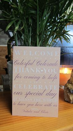 a welcome card sitting on top of a wooden table next to a potted plant