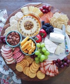 a wooden platter filled with cheese, crackers and fruit