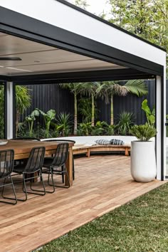 an outdoor dining area with wooden decking and black chairs, surrounded by greenery