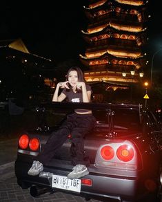 a woman sitting on the back of a car in front of a tall building at night