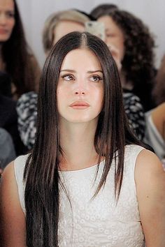 a woman with long brown hair sitting in front of a group of people looking at the camera