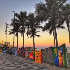 a row of palm trees next to the ocean with colorful clothing hanging on it's sides