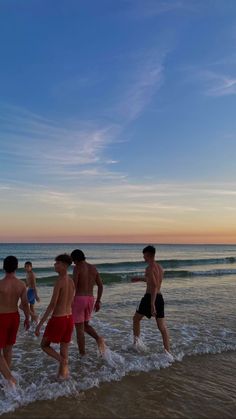 a group of people walking into the ocean at sunset