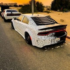 two cars are parked on the side of the road with their hoods down and covered in black dots