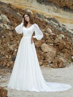 a woman in a white wedding dress standing on the beach with her arms behind her head