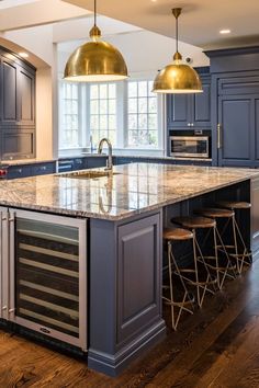 a large kitchen with blue cabinets and marble counter tops, two pendant lights over the island