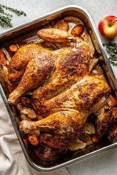 a roasting pan filled with chicken, potatoes and apples next to an apple on the side