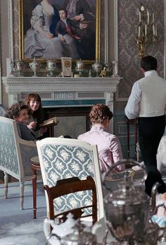 people are sitting in chairs around a table with a painting on the wall behind them